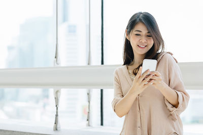 Young woman using phone while standing on laptop