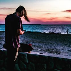 Woman standing on beach against sky during sunset