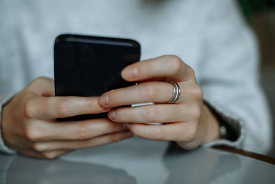 Young brunette woman in a gray jumper uses a mobile phone in a cafe