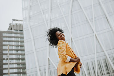 Smiling female entrepreneur with eyes closed standing against office building