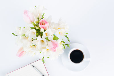 Directly above shot of black coffee with diary and flowers over white background