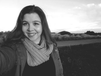 Portrait of smiling young woman on field against sky