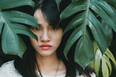 Close-up portrait of young woman by leaves at park