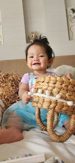 Front shot of smiling baby holding a weave basket on a bed at home