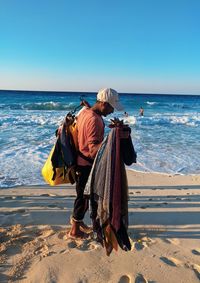 Man holding umbrella at beach against clear sky
