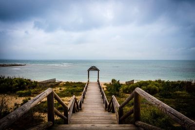 Wooden boardwalk leading towards sea against sky