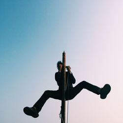 Low angle view of man climbing pole against clear sky