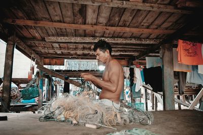 Shirtless man working with wool