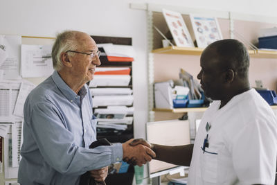 Smiling senior patient shaking hand with mature male doctor after visit in clinic