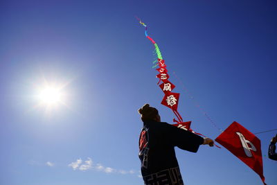 Low angle view of woman flying kite against blue sky