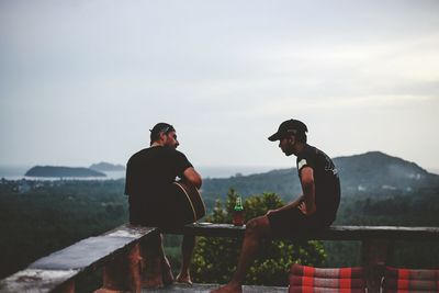 Men sitting on mountain against sky
