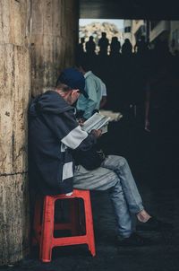 Full length of man reading book while sitting on stool