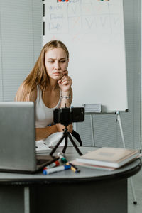 Portrait of young woman using phone while sitting on table