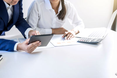 Midsection of colleagues using digital tablet at desk in office