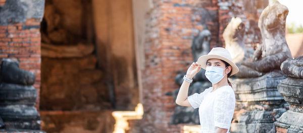 Portrait of woman wearing mask standing against ancient temple