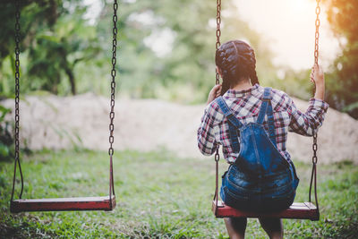 Rear view of woman sitting on swing at park