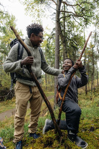 Smiling boy kneeling and looking at father holding firewood in forest during vacation