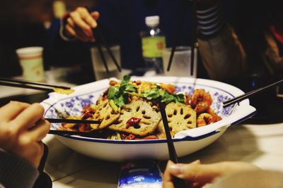 Cropped hands holding chopsticks by bowl of food