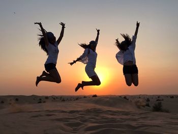 Low angle view of silhouette people jumping on sand against sky