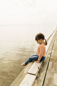 Full length side view of girl sitting on pier at beach