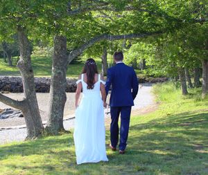Rear view of newlywed couple walking on grassy field at park