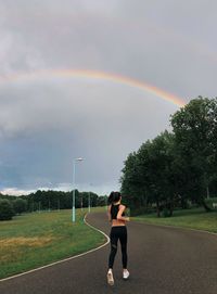 Full length of man standing on field against rainbow in sky