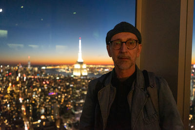 Portrait of young man standing against illuminated city at night