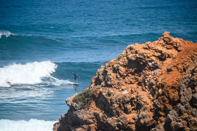 High angle view of man surfing in sea by rocks