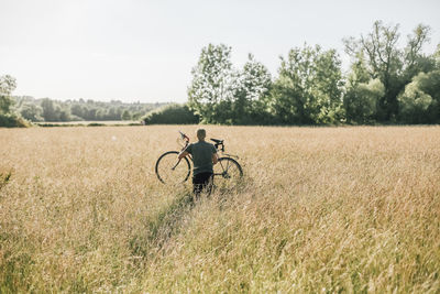 Young man carrying his bike, field