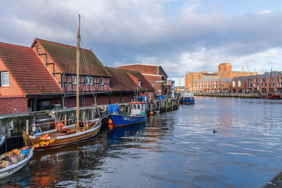 Boats in canal by buildings against sky