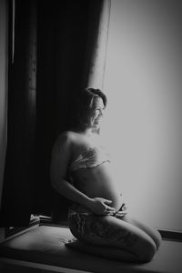 Smiling pregnant woman kneeling by window at home