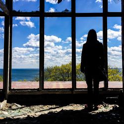 Full length rear view of silhouette woman looking sea through abandoned window