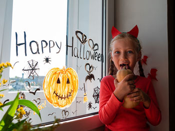 Child chewing pumpkin painting on window preparing to celebrate halloween little girl decorates room