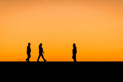 Silhouette people standing against orange sky