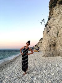 Young man standing on rock at beach against sky