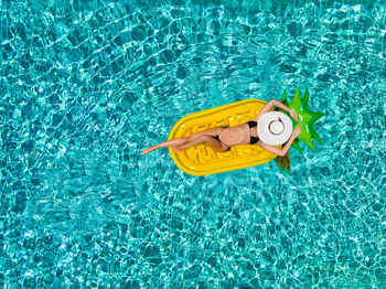 Directly above shot of woman lying pool raft while floating on swimming pool