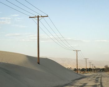 Electricity pylon by road against sky