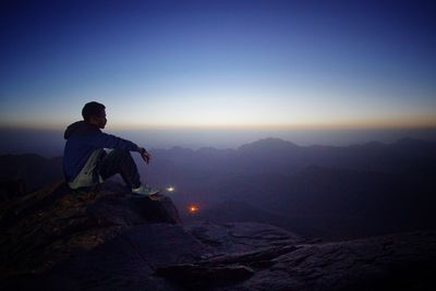 Man sitting on mountain against sky during sunset