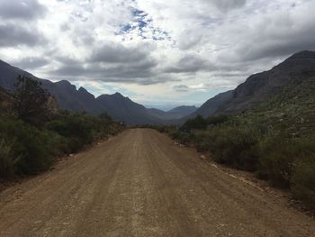 Dirt road against cloudy sky