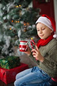 Smiling boy holding candy cane while sitting at home during christmas