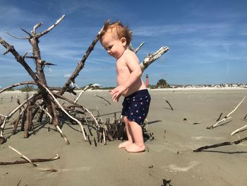 Full length of boy standing by driftwood on sand at beach against sky