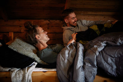 Smiling couple with blankets relaxing on bed in cottage