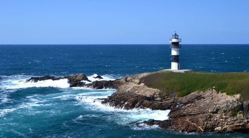 Illa pancha lighthouse on cliff by sea against clear sky