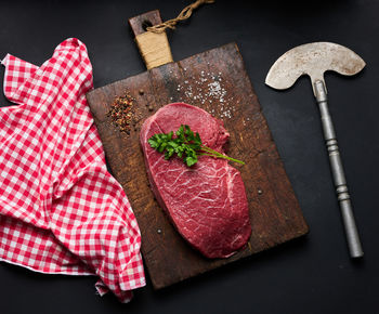 Raw beef tenderloin lies on a cutting board and spices for cooking on a black table, top view