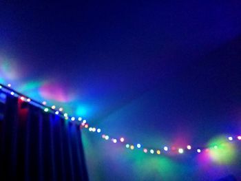 Low angle view of illuminated lighting equipment hanging against blue sky