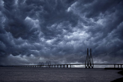 Bridge over calm sea against cloudy sky