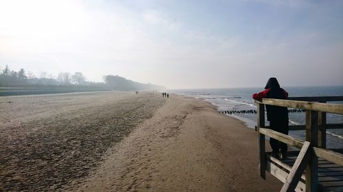 Rear view of man looking at beach while standing on lookout tower against sky