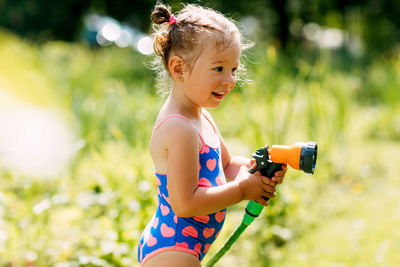 Charming baby girl waters plants with a hose in the garden in the backyard of the house 