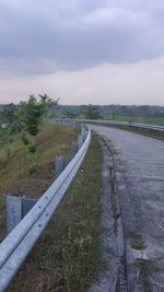 Empty road amidst field against sky