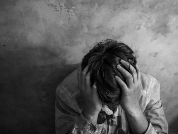 Man sitting with head in hands against wall 